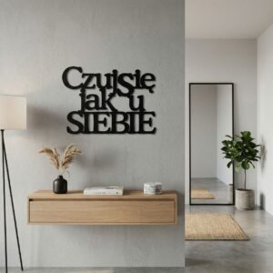 Czarny, wycinany laserowo napis metalowy Czuj się jak u siebie, zamontowany na jasnej ścianie nad minimalistyczną, białą kanapą w nowoczesnym salonie.