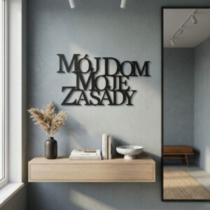 Czarny metalowy napis Mój dom moje zasady zamontowany na beżowej ścianie nad nowoczesną szarą kanapą w przytulnym, jasnym salonie z roślinami.