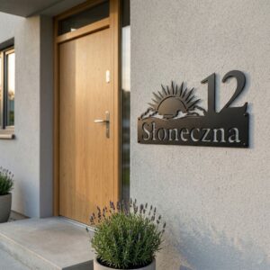 Metalowa tabliczka adresowa z numerem domu i wzorem wschodzącego słońca, zamontowana na jasnej elewacji obok drewnianych drzwi.