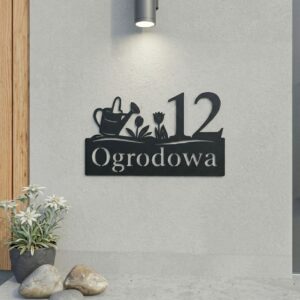 Zbliżenie na czarny, wycinany laserowo numer na dom z nazwą ulicy i ozdobnym motywem ogrodniczym: konewką oraz tulipanami