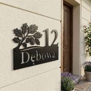 Nowoczesny numer na dom z nazwą ulicy i ozdobną gałązką dębu z żołędziami, czarna stal na jasnej ścianie budynku