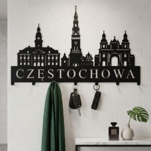 Czarny wieszak ścienny z motywem panoramy Częstochowy z powieszonymi kurtkami i płaszczami, zamontowany na jasnej ścianie nad minimalistyczną ławeczką.