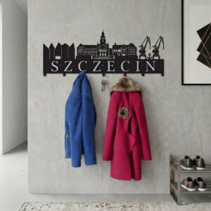 Czarny, metalowy wieszak ścienny z wyciętymi zabytkami Szczecina i napisem, zawieszony na jasnej ścianie z powieszonymi ubraniami.