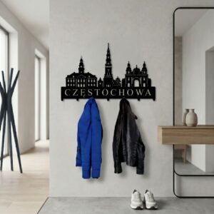 Solidny, wycinany z metalu wieszak na odzież wierzchnią z architekturą Częstochowy, zawieszony na ścianie w przytulnym, eleganckim korytarzu z roślinami.