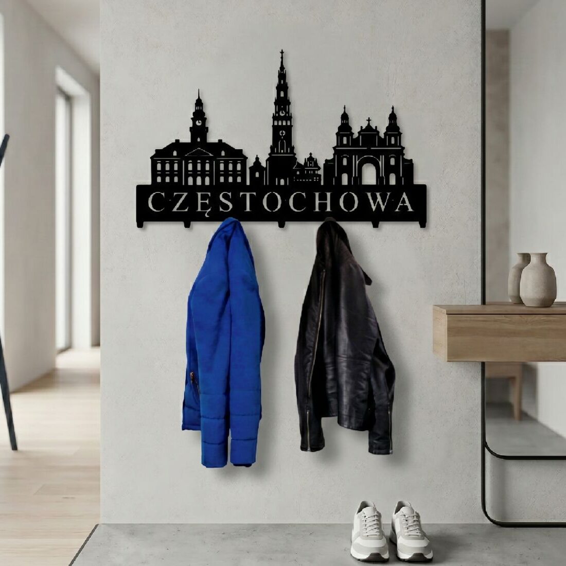 Solidny, wycinany z metalu wieszak na odzież wierzchnią z architekturą Częstochowy, zawieszony na ścianie w przytulnym, eleganckim korytarzu z roślinami.