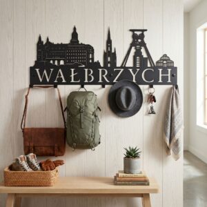Solidny wieszak metalowy Wałbrzych z motywem Zamku Książ i Starej Kopalni, zamontowany na ścianie z desek. Na wieszaku wiszą plecak, kapelusz i szalik.