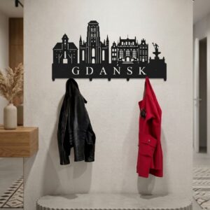 Czarny, metalowy wieszak na ubrania z napisem Gdańsk i zarysami gdańskich zabytków, wiszący na jasnej ścianie działowej z zawieszoną czarną kurtką i czerwonym płaszczem.