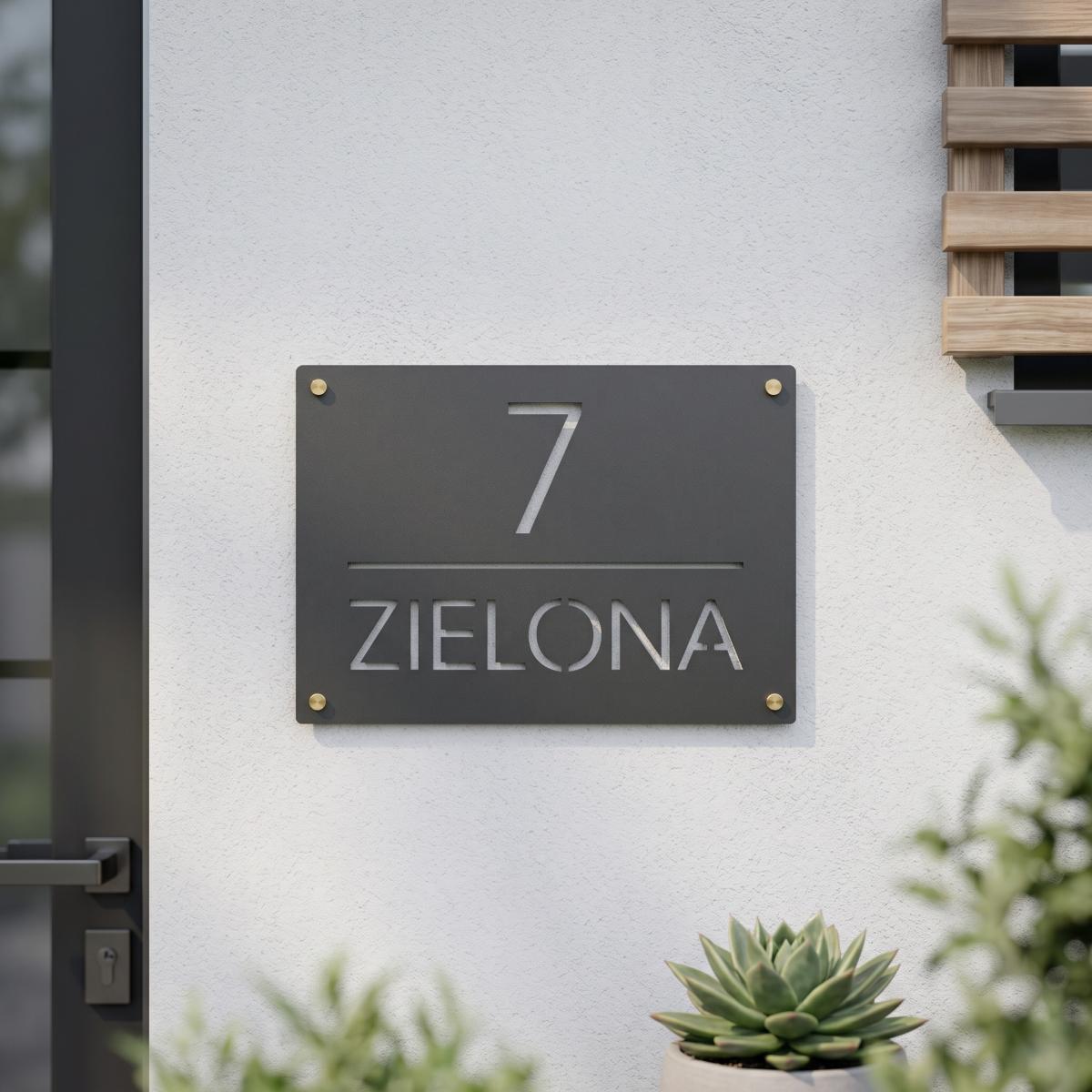 Szara metalowa tabliczka z numerem 7 i nazwą ulicy Zielona zamontowana na białej elewacji budynku
