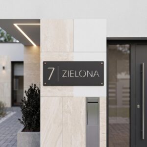 Ciemna metalowa tabliczka adresowa Model Linea z numerem 7 i nazwą ulicy Zielona zamontowana na jasnej elewacji obok skrzynek i drzwi